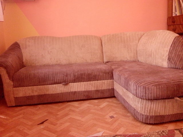 Narożnik tapicerowany sztruksem w odcieniach beżu i brązu, z widoczną fakturą materiału i drewnianą podłogą w jodełkę.