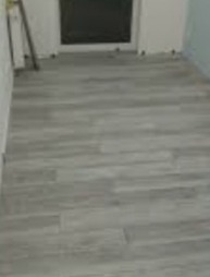 Ułożona szara podłoga z płytek imitujących drewno w trakcie remontu, widoczne płytki dystansowe i narzędzia oparty o ścianę.