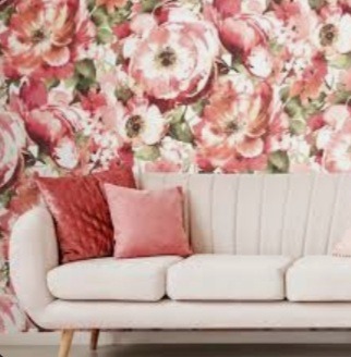 Jasnoszara sofa z dwoma poduszkami w odcieniach różu i bordo na tle ściany pokrytej tapetą w kwiaty w stylu vintage.