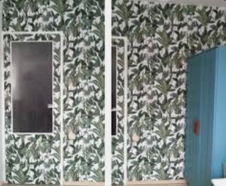 Ściana pokryta tapetą w tropikalne liście, biała rama okalająca ciemne okno, błękitna szafa w rogu pomieszczenia.