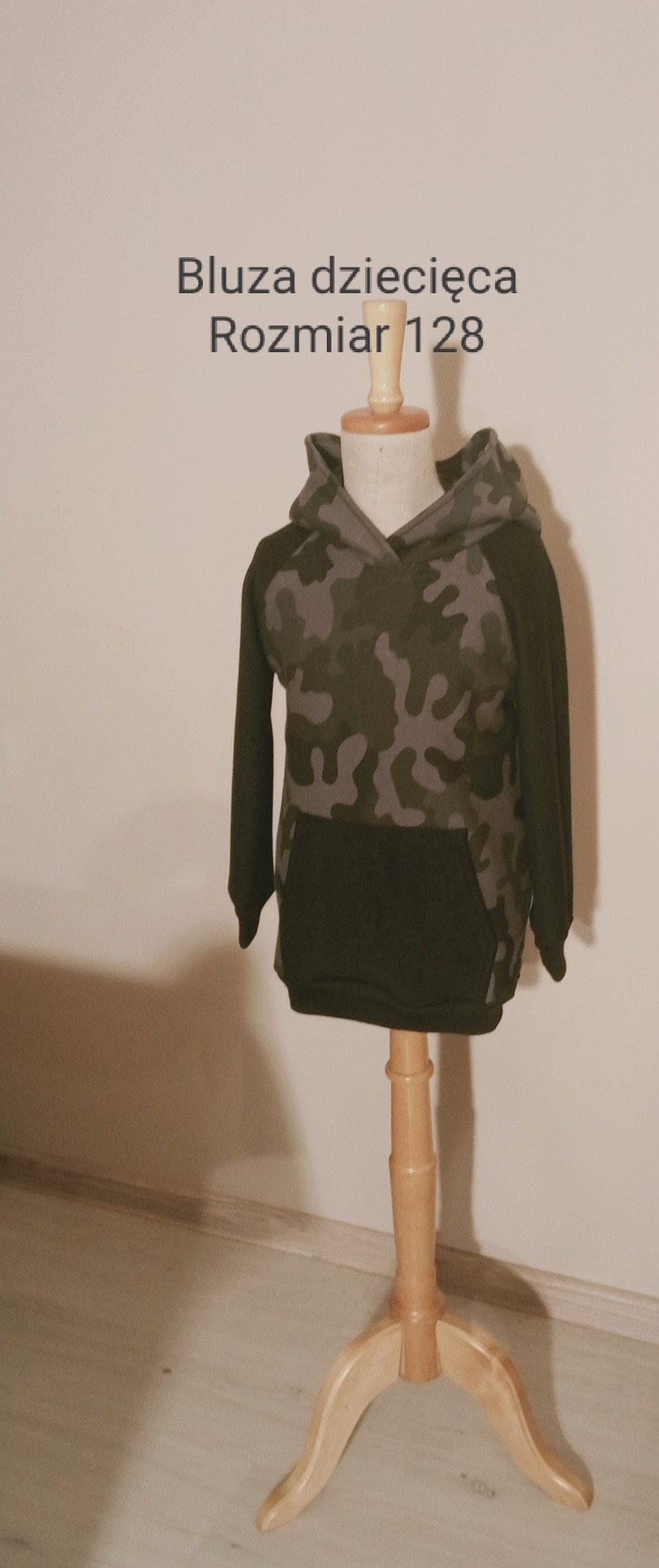 Dziecięca bluza z kapturem w odcieniach zieleni i szarości z wzorem kamuflażu, prezentowana na drewnianym manekinie o rozmiarze 128.