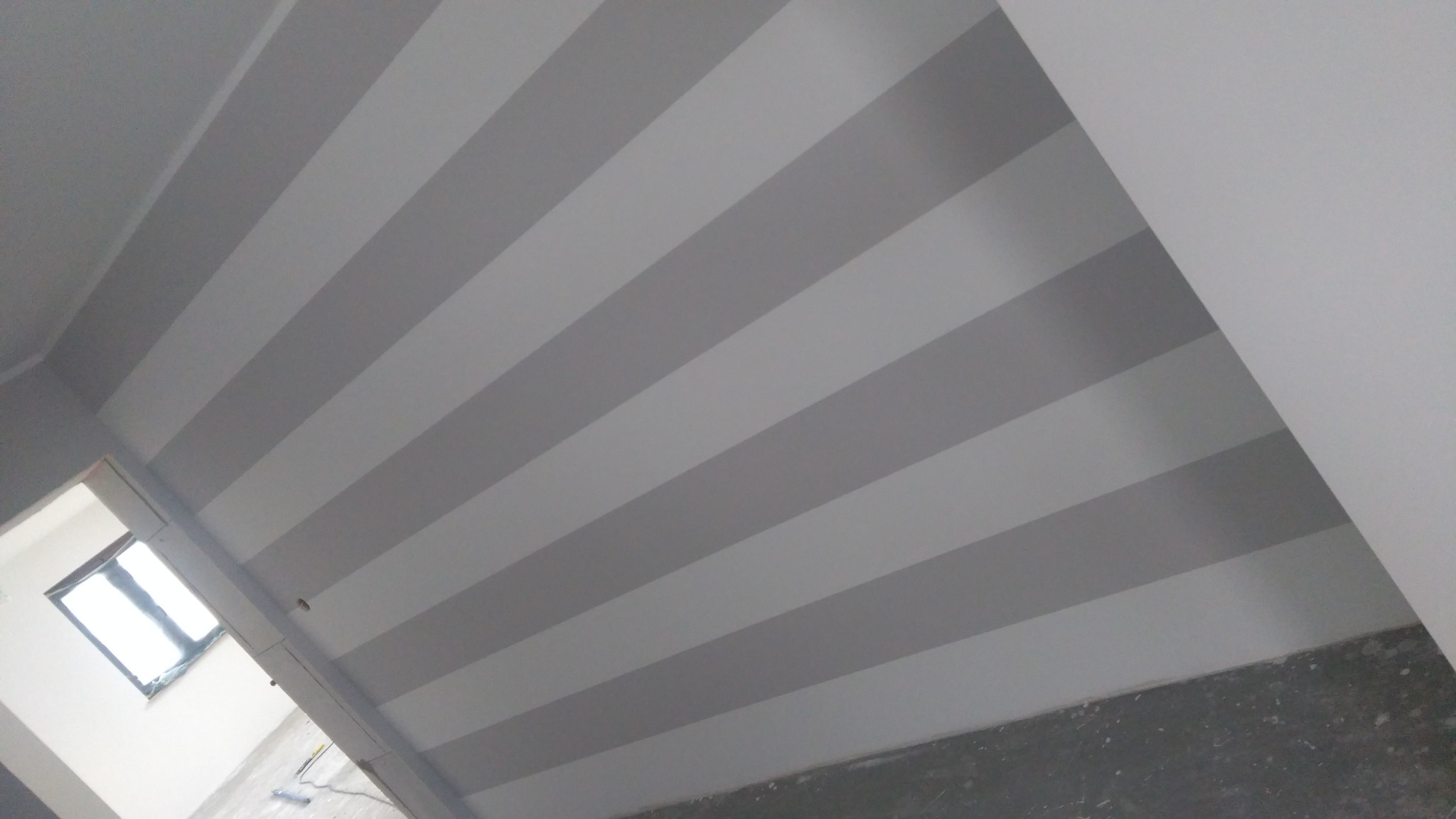 Pomalowany sufit w biało-szare pasy, widok z dołu, fragment okna w tle po lewej stronie.