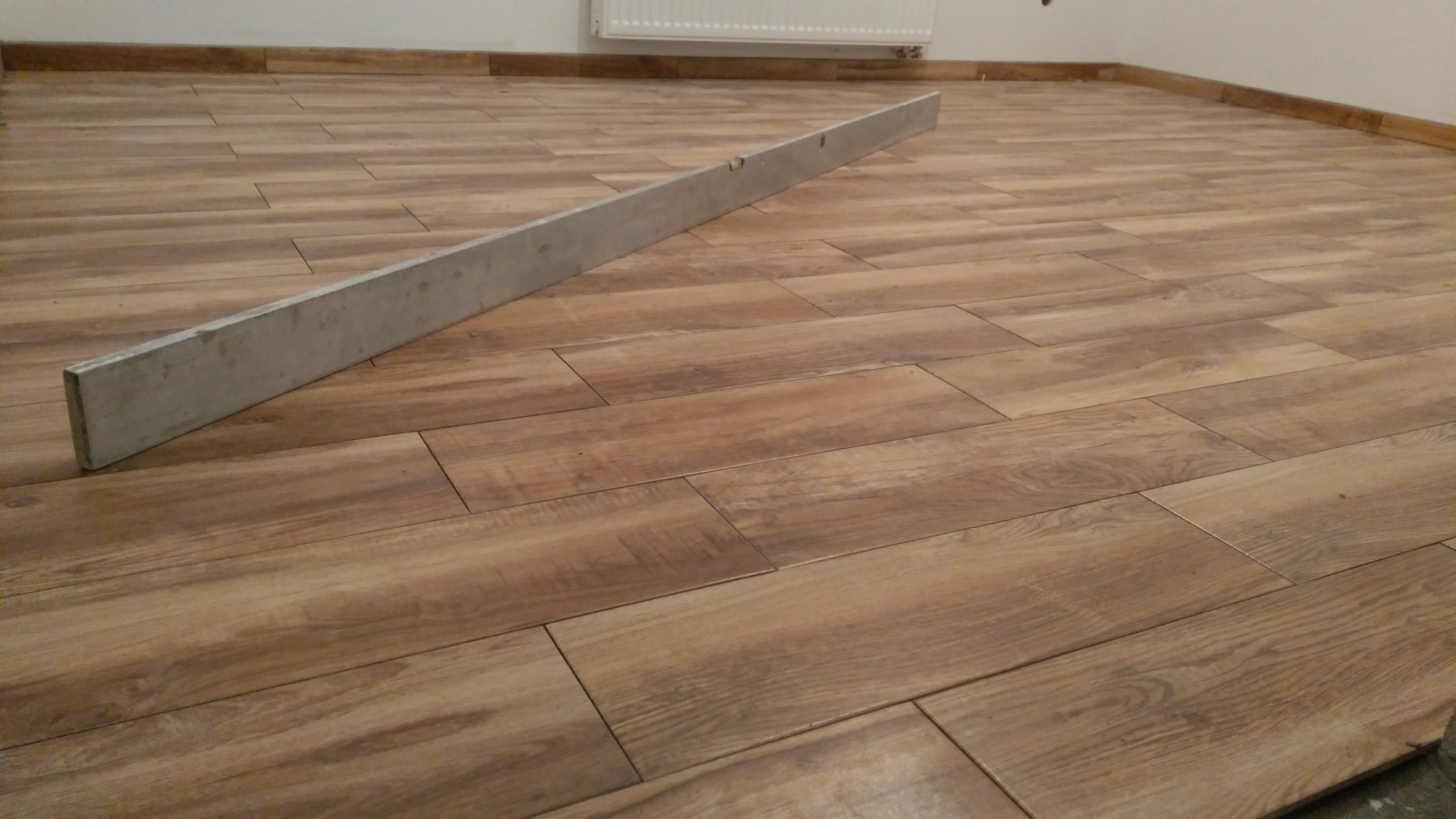 Ułożona podłoga z płytek imitujących drewno, z widoczną poziomicą aluminiową na powierzchni, sprawdzającą równość ułożenia.