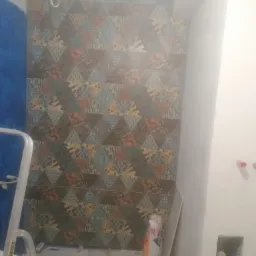 Układanie dekoracyjnych, trójkątnych płytek glazurniczych na ścianie w łazience, widoczny worek z klejem i drabina.