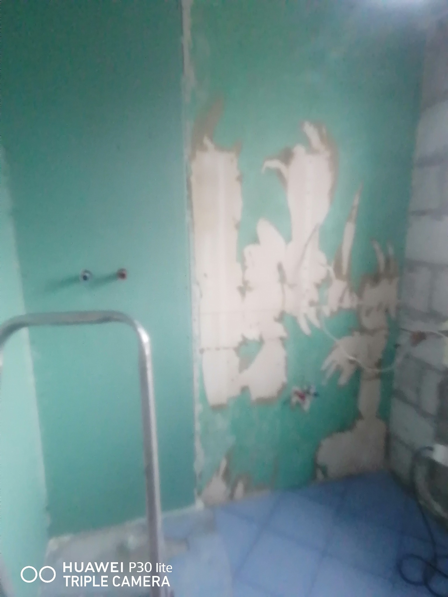 Przygotowanie ściany do prac wykończeniowych w łazience w Wałczu: usunięta stara farba, widoczne fragmenty tynku i instalacja wodna, drabina malarska w rogu pomieszczenia.