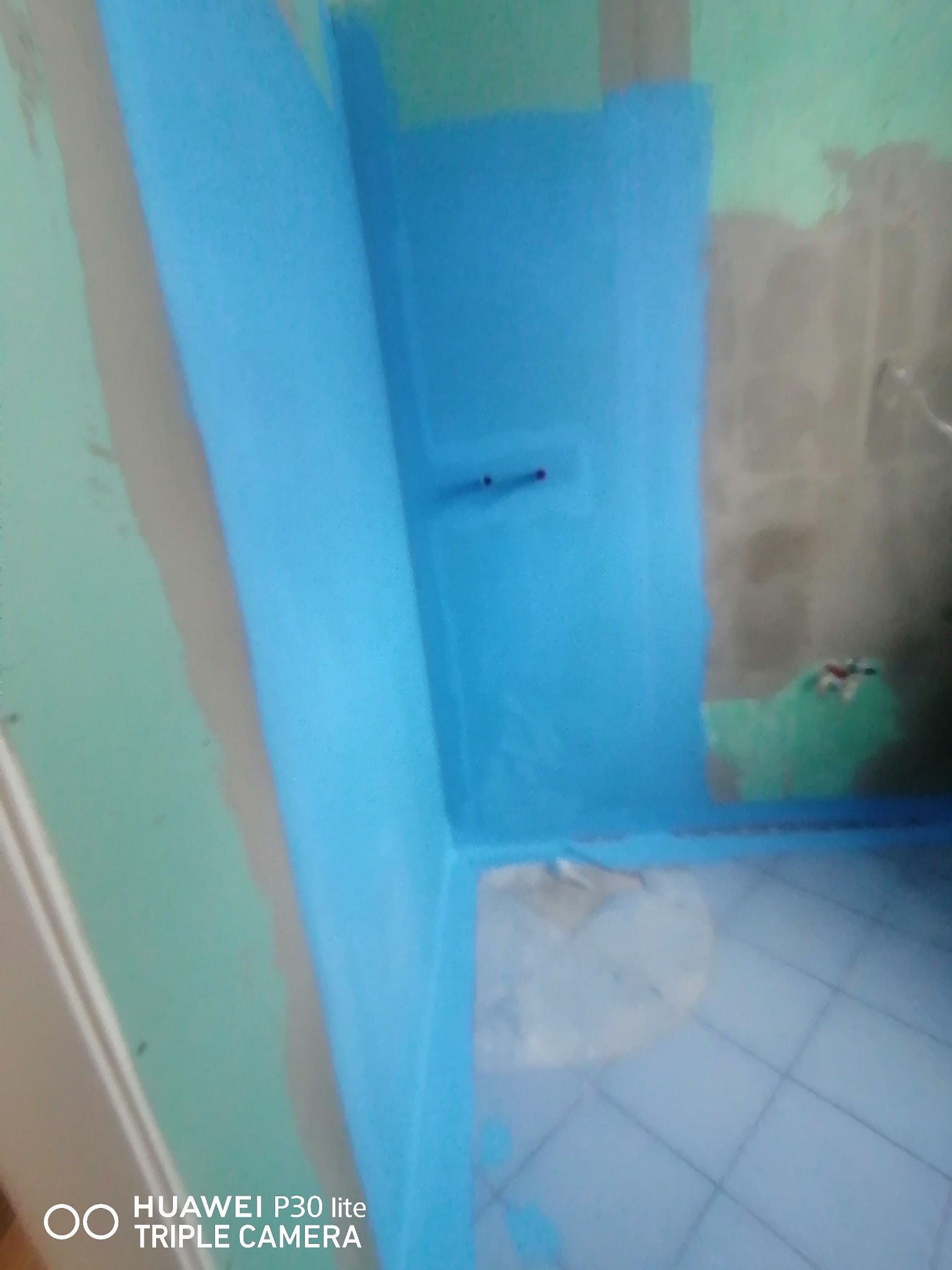 Hydroizolacja w narożniku łazienki, nałożona na ściany i podłogę, widoczne przygotowane podłoże pod płytki.