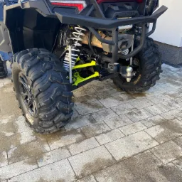 Częściowo widoczny czarny quad Polaris z oponami terenowymi na kostce brukowej, z akcentami w kolorze limonki na zawieszeniu.