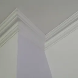 Wykończony narożnik sufitu z ozdobną, białą listwą przysufitową, widok z dołu na połączenie dwóch ścian w jasnym, neutralnym wnętrzu.
