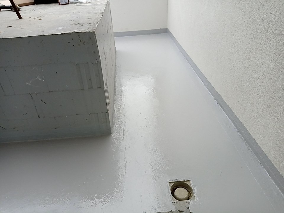 Jasnoszara, błyszcząca posadzka w trakcie wylewania, widoczny betonowy element konstrukcyjny i odpływ podłogowy.