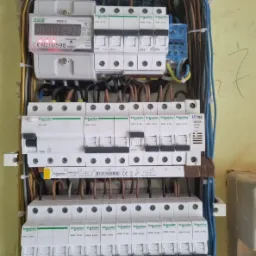 Rozdzielnica elektryczna z zamontowanym licznikiem i zabezpieczeniami nadprądowymi firmy Schneider, widoczne okablowanie i oznaczenia faz.