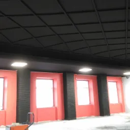 Wnętrze biura w trakcie prac wykończeniowych: czarny, kasetonowy sufit, czerwone wnęki okienne z czarnymi kolumnami, widoczny sprzęt malarski.