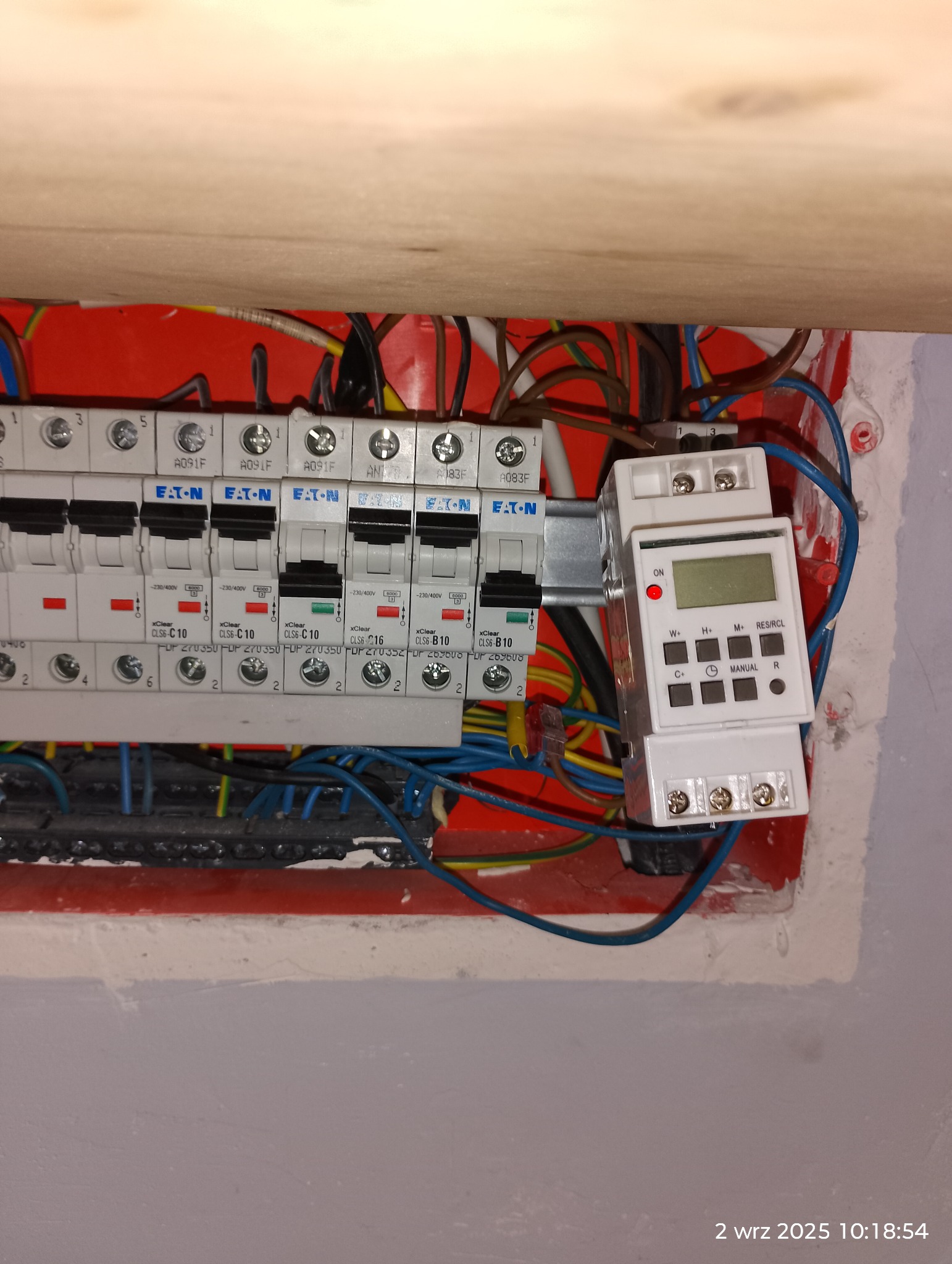 Rozdzielnica elektryczna z zamontowanym programatorem czasowym, widoczne bezpieczniki Eaton i okablowanie wewnątrz skrzynki. Instalacja elektryczna w budynku.