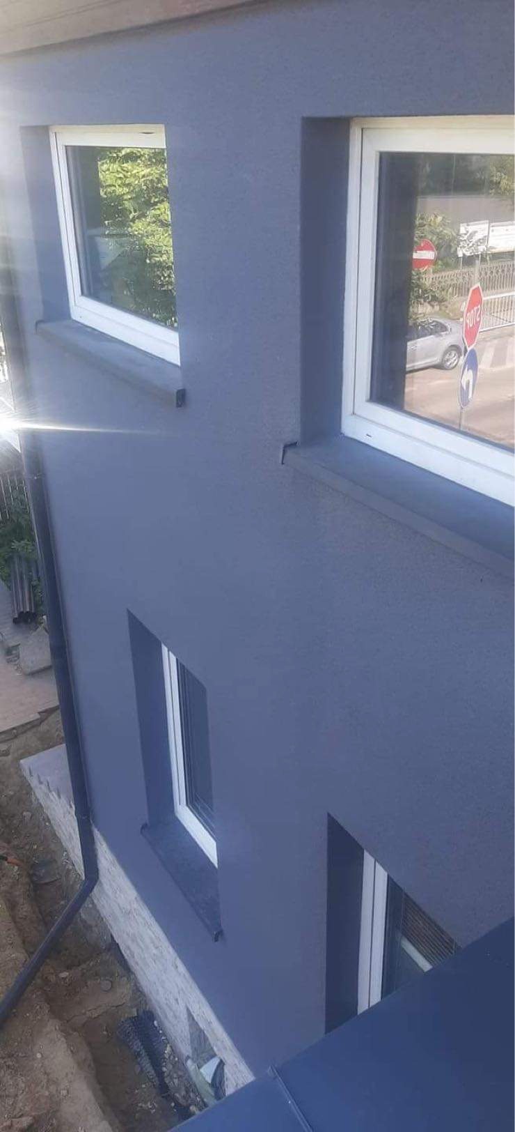 Szara elewacja budynku z białymi oknami, widok z góry, z fragmentem dachu i rynną.