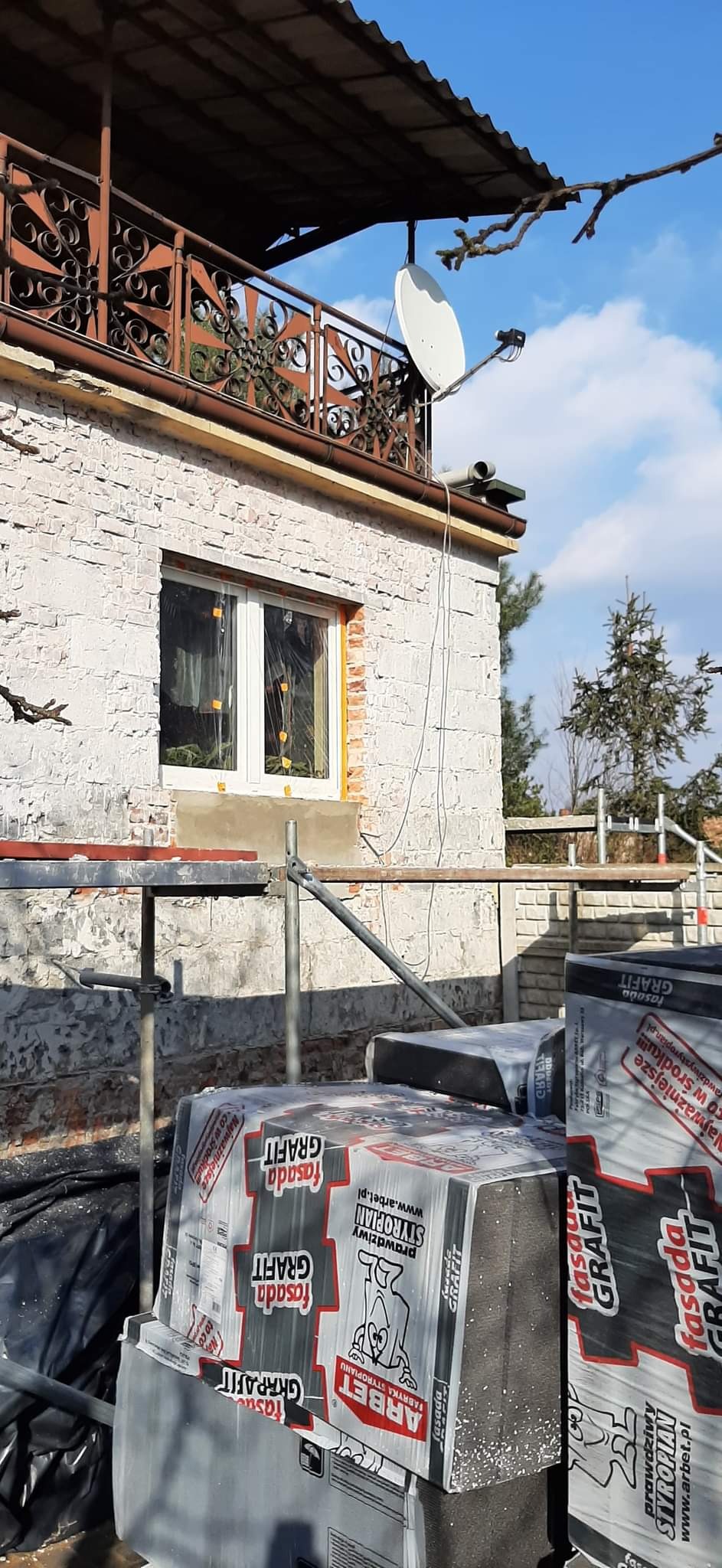 Dom w trakcie ocieplania, widoczne rusztowania, okno zabezpieczone folią, oraz paczki styropianu grafitowego ARBET Fasada Grafit.