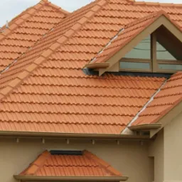 Dom z nowym, pomarańczowym dachem z dachówki ceramicznej, widoczne okno dachowe w trójkątnym szczycie.