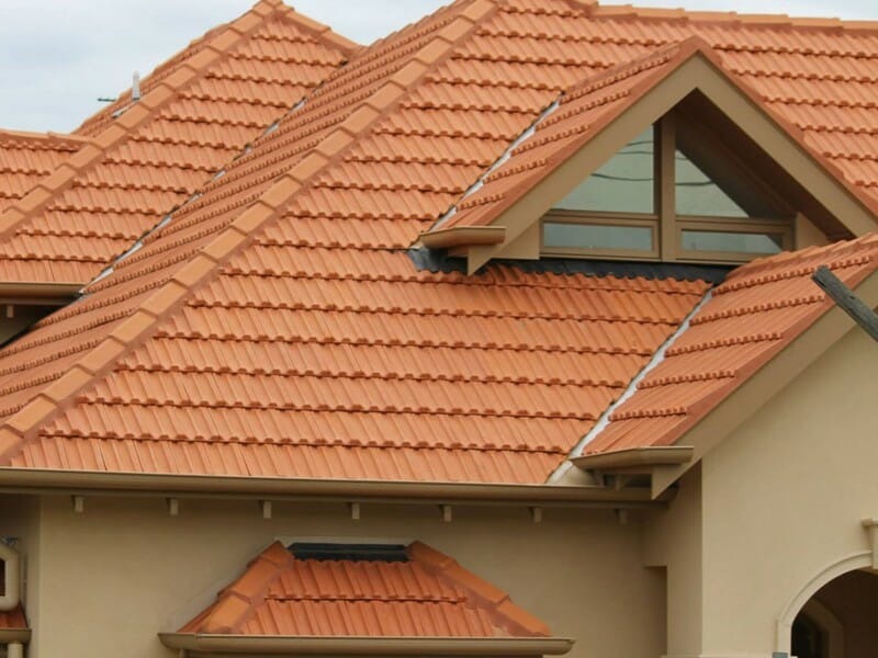 Dom z nowym, pomarańczowym dachem z dachówki ceramicznej, widoczne okno dachowe w trójkątnym szczycie.