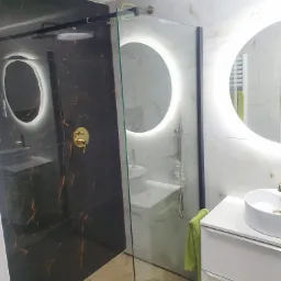 Nowoczesna łazienka z kabiną prysznicową typu walk-in, czarną armaturą i podświetlanymi lustrami w kształcie okręgów.