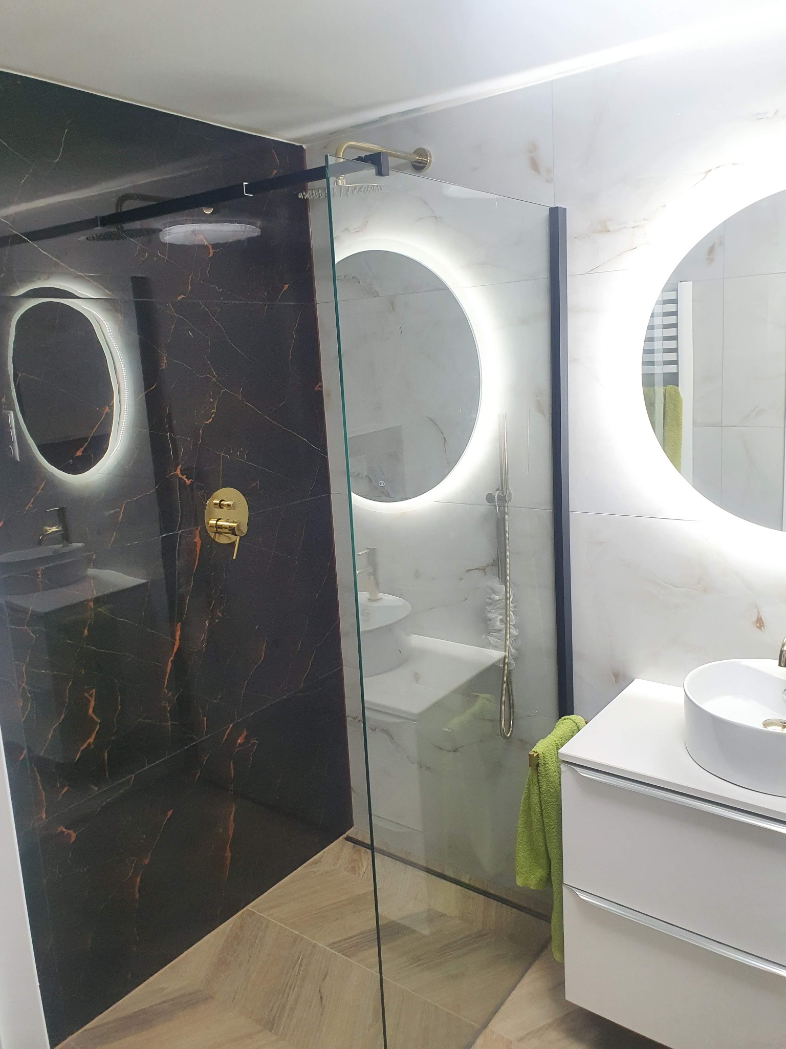 Nowoczesna łazienka z kabiną prysznicową typu walk-in, czarną armaturą i podświetlanymi lustrami w kształcie okręgów.