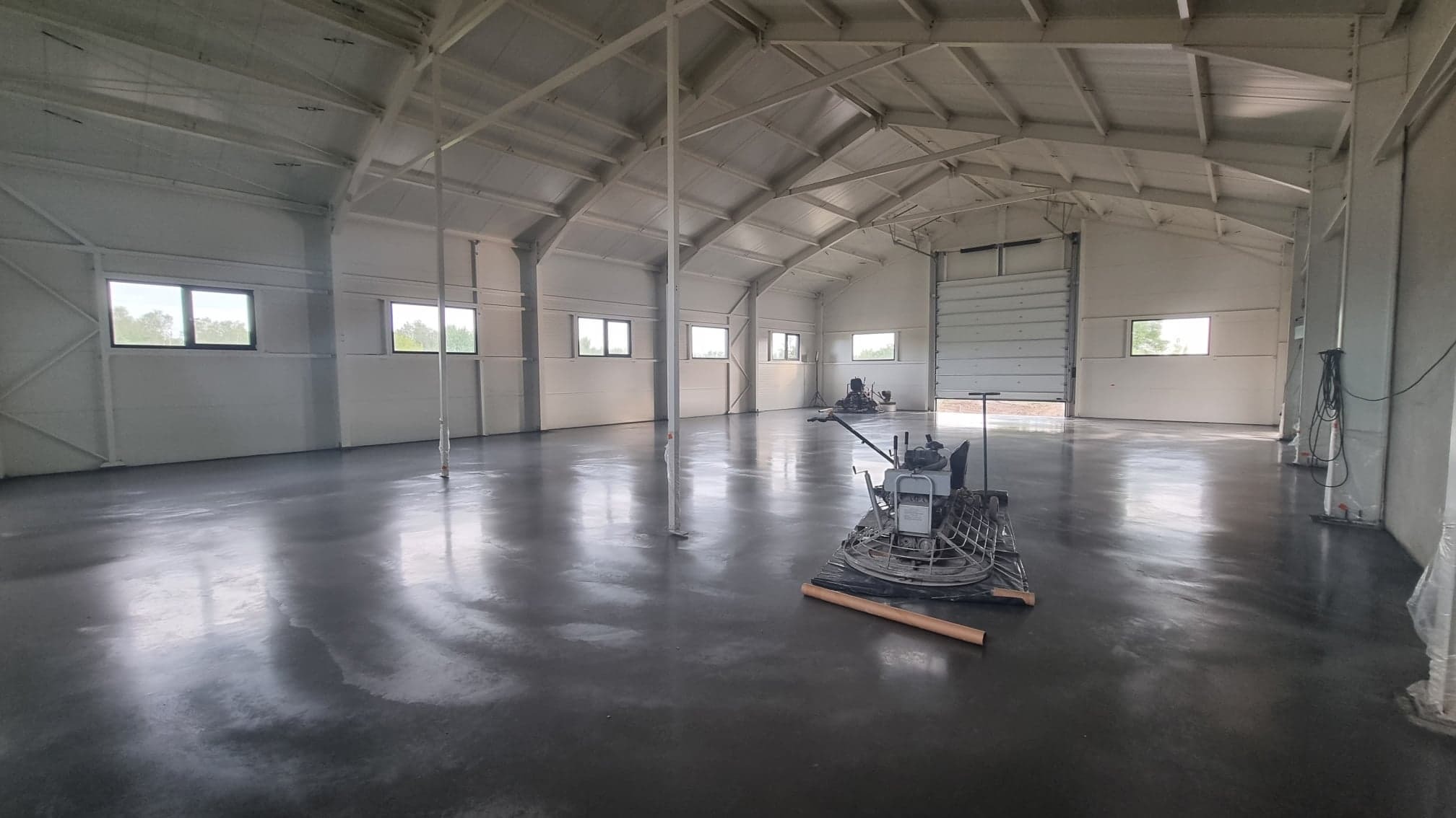 Wnętrze hali z wypolerowaną, błyszczącą posadzką betonową i maszyną do polerowania betonu w tle.