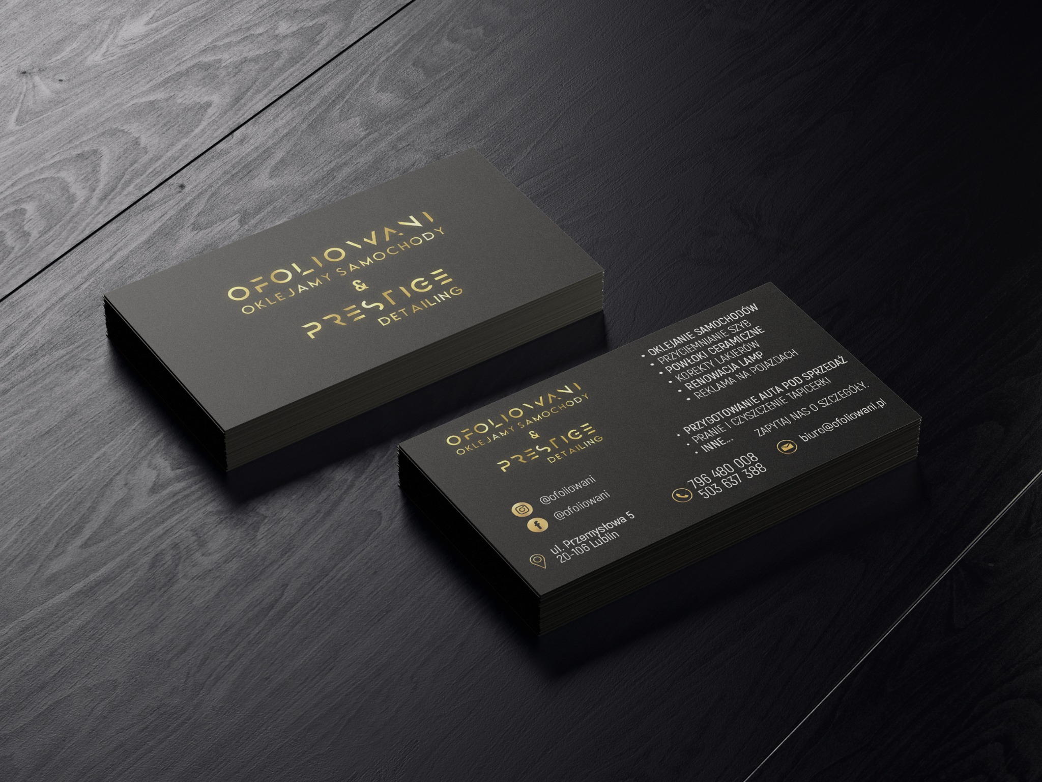 Stos wizytówek firmy Ofoliowani, specjalizującej się w oklejaniu samochodów i detailingu, ułożony na ciemnym drewnianym tle, z widocznym logo i danymi kontaktowymi.