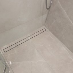 WR Remont dla Ciebie - Wykończona kabina prysznicowa w Katowicach z odpływem liniowym i marmurowymi płytkami. Minimalistyczny design, jasne barwy, nowoczesne rozwiązanie odprowadzania wody.