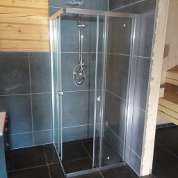 WR Remont dla Ciebie - Kabina prysznicowa z chromowaną armaturą na tle ciemnych płytek i drewnianej boazerii, widok z boku, nowoczesny design.