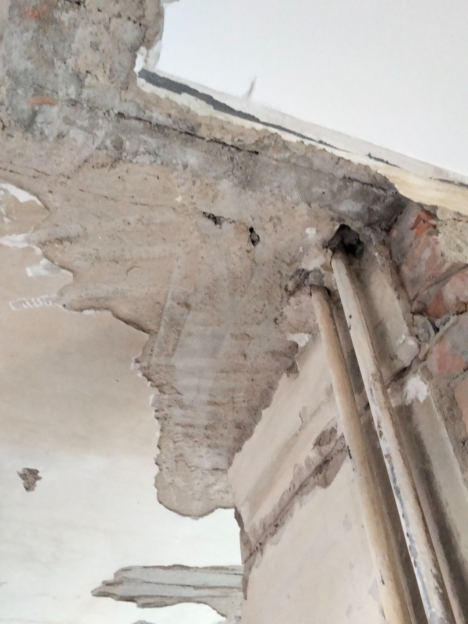 Fragment ściany z odsłoniętą cegłą i instalacją hydrauliczną po usunięciu fragmentu tynku i betonu.