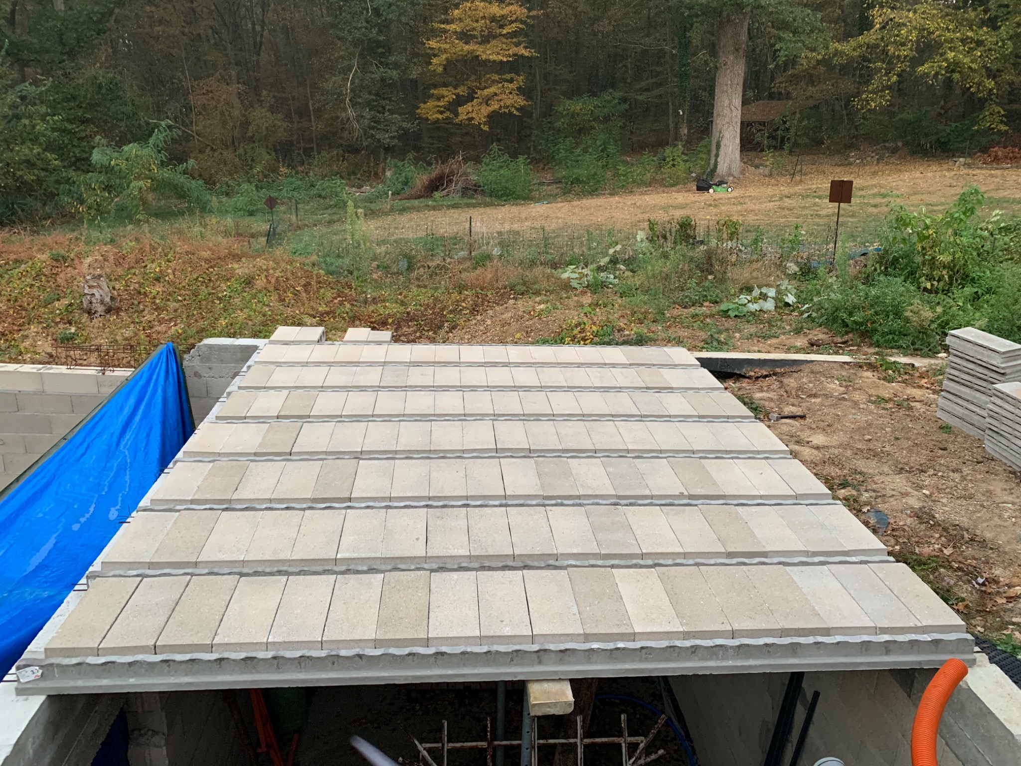 Budowa stropu Teriva w Nowęcinie, widoczne elementy stropowe ułożone na ścianach fundamentowych, w tle drzewa i niebieska plandeka.