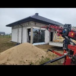 Montaż okna za pomocą specjalistycznego dźwigu przyssawkowego na budowie domu jednorodzinnego w stanie surowym.