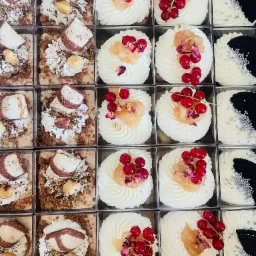 Różnorodne mini desery w przezroczystych pudełkach: kremowe z owocami, czekoladowe z orzechami i biało-czarne z srebrnymi kuleczkami.