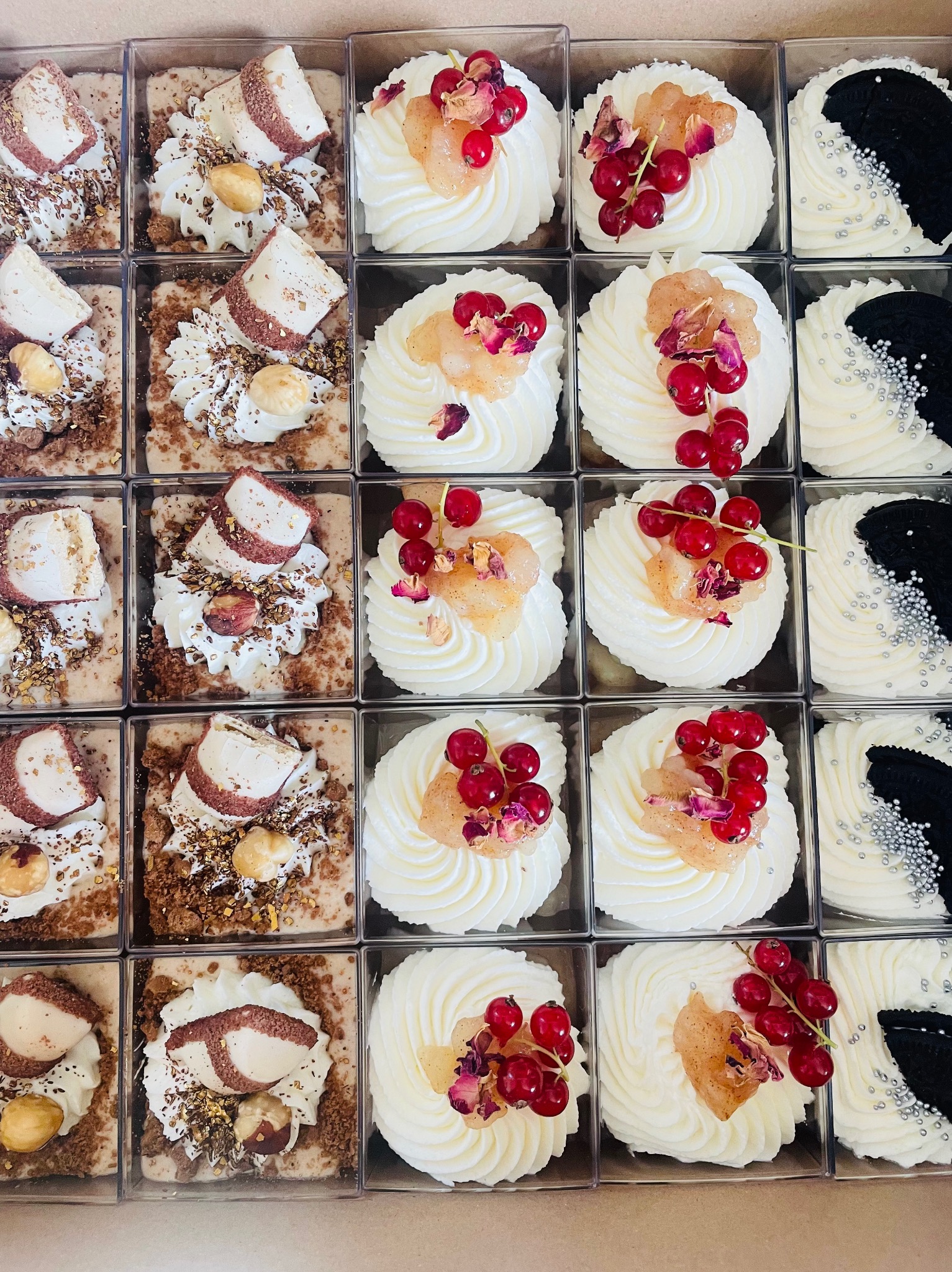 Różnorodne mini desery w przezroczystych pudełkach: kremowe z owocami, czekoladowe z orzechami i biało-czarne z srebrnymi kuleczkami.