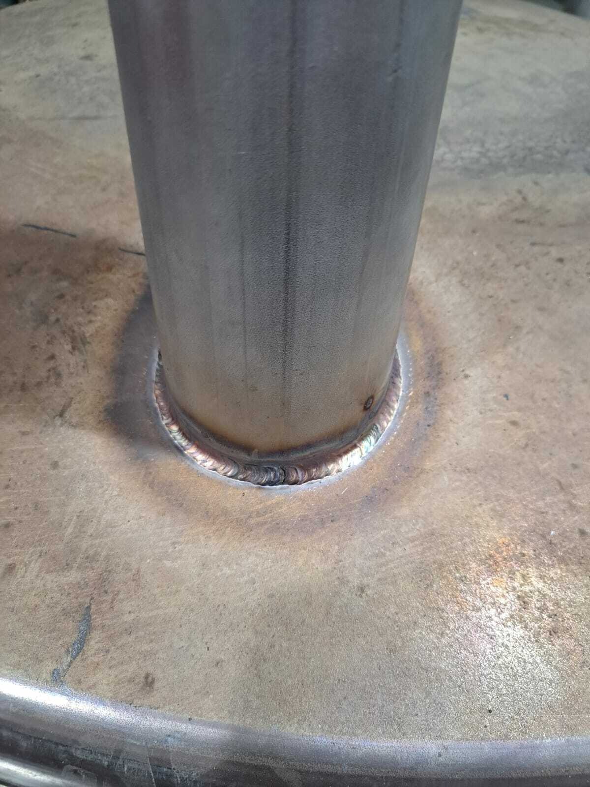 Metalowy słup przyspawany do metalowej powierzchni, widoczny spaw w zbliżeniu, z lekkimi przebarwieniami termicznymi.