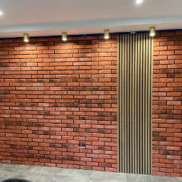 Ściana z cegły klinkierowej z pionowym panelem dekoracyjnym z drewnianych listew, oświetlona punktowymi lampami sufitowymi.