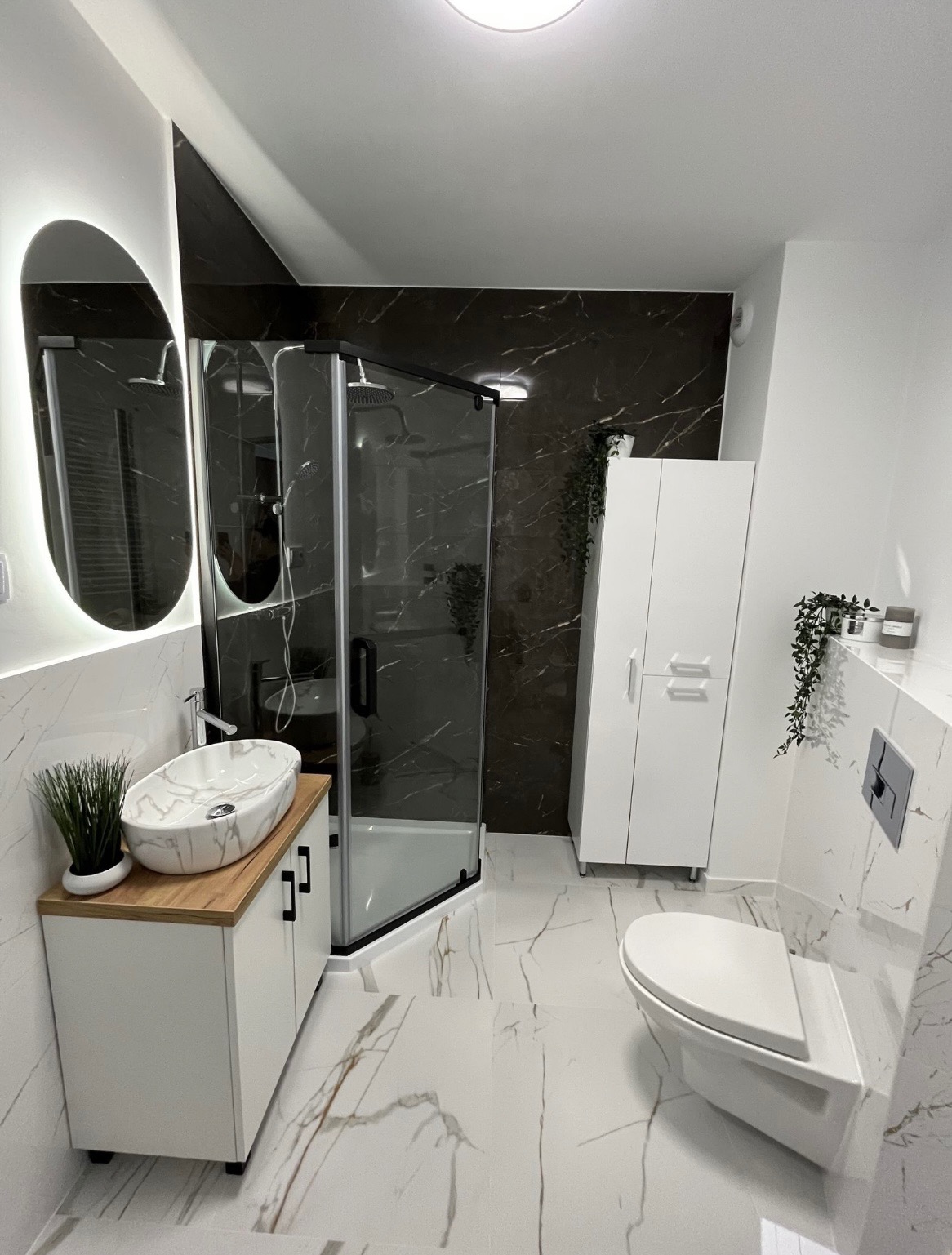 Nowoczesna łazienka z kabiną prysznicową typu walk-in, umywalką nablatową z marmurowym wzorem na drewnianym blacie, białymi szafkami i płytkami imitującymi marmur na podłodze i ścianach.