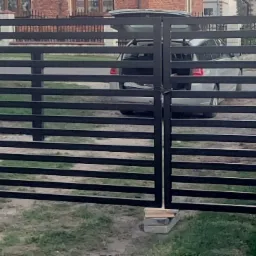 Nowoczesna, pozioma brama wjazdowa i furtka z czarnych, płaskich profili, widok z zewnątrz na posesję z zaparkowanym samochodem.