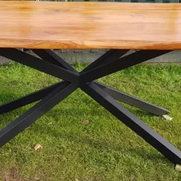 Stół z blatem z jasnego drewna o nieregularnych krawędziach i metalową podstawą w kształcie gwiazdy, wykonany w Bełchatowie.