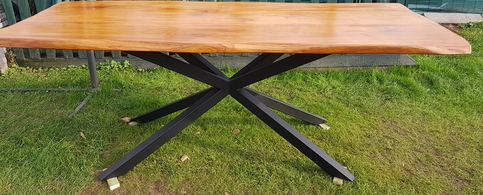 Stół z blatem z jasnego drewna o nieregularnych krawędziach i metalową podstawą w kształcie gwiazdy, wykonany w Bełchatowie.