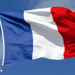 Flaga Francji powiewająca na wietrze na tle błękitnego nieba z chmurami.