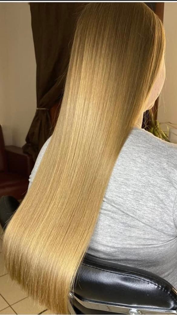 Długie, proste, blond włosy po koloryzacji, widoczne z tyłu na krześle fryzjerskim, z delikatnym połyskiem.