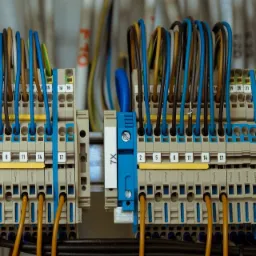 Dwa bloki zaciskowe z podłączonymi przewodami w różnych kolorach, zamontowane na szynie DIN, z widocznymi oznaczeniami numerów zacisków i etykietami X9 i 7X.