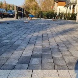 Ułożona, szara kostka brukowa na podjeździe w Jaworznie, widok z niskiej perspektywy, brama w tle, częściowo zacieniona powierzchnia.