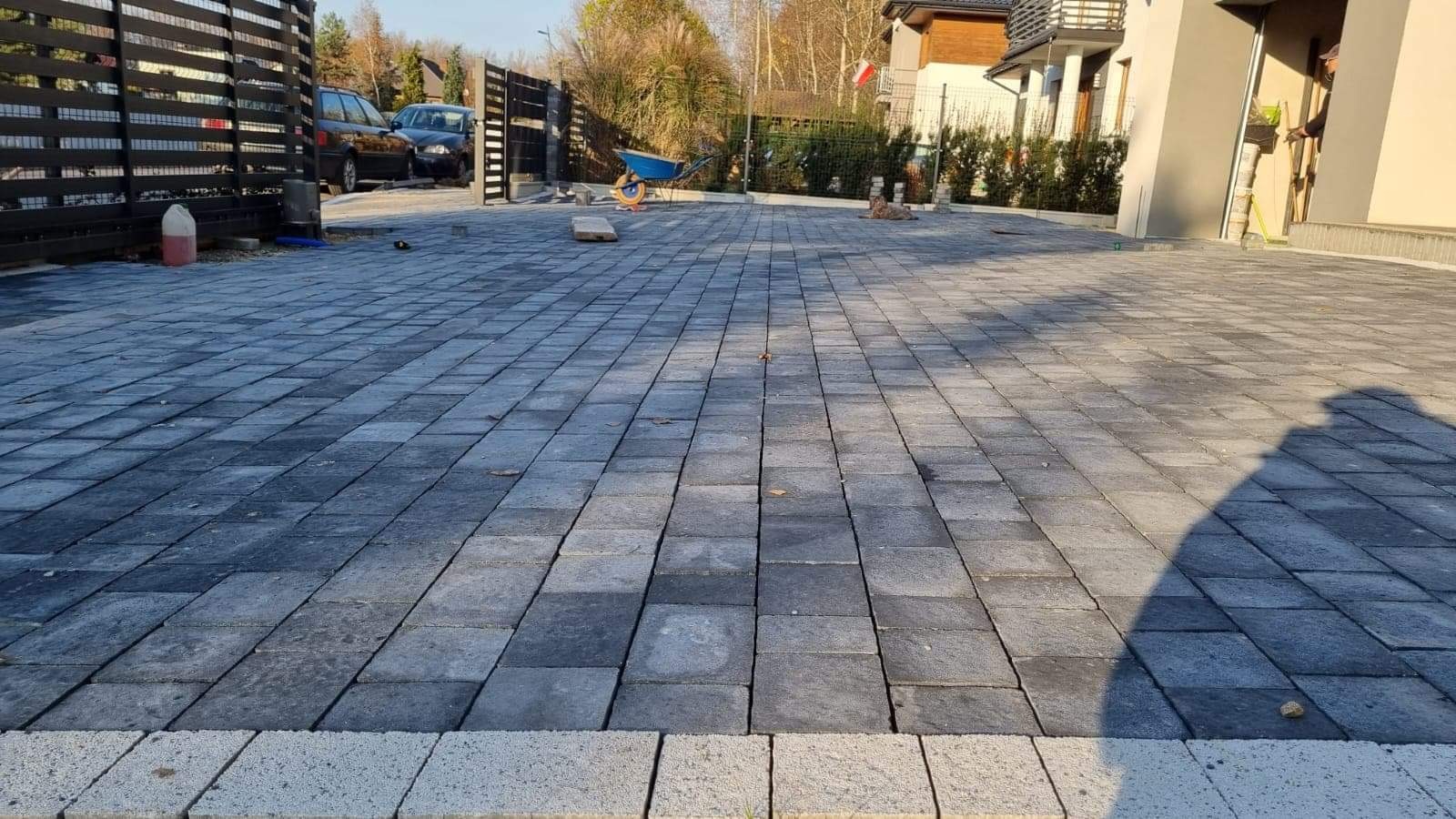 Ułożona, szara kostka brukowa na podjeździe w Jaworznie, widok z niskiej perspektywy, brama w tle, częściowo zacieniona powierzchnia.