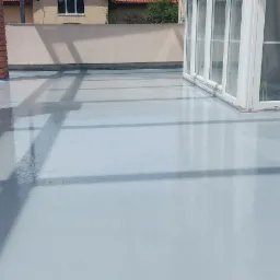 Jasnoszara, błyszcząca powierzchnia balkonu po nałożeniu powłoki, widoczne detale wykończenia przy ścianie i słupkach z cegły.