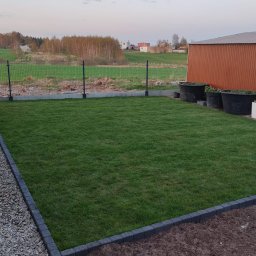 Paweł Iwanowski PafiNature - Świeżo założony trawnik z rolki, obrzeża z kostki, widoczne duże donice i ogrodzenie panelowe w tle.