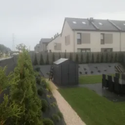 Nowo założony ogród z trawnikiem, ścieżką z jasnych kamieni i podwyższoną rabatą obsadzoną tujami wzdłuż ogrodzenia.