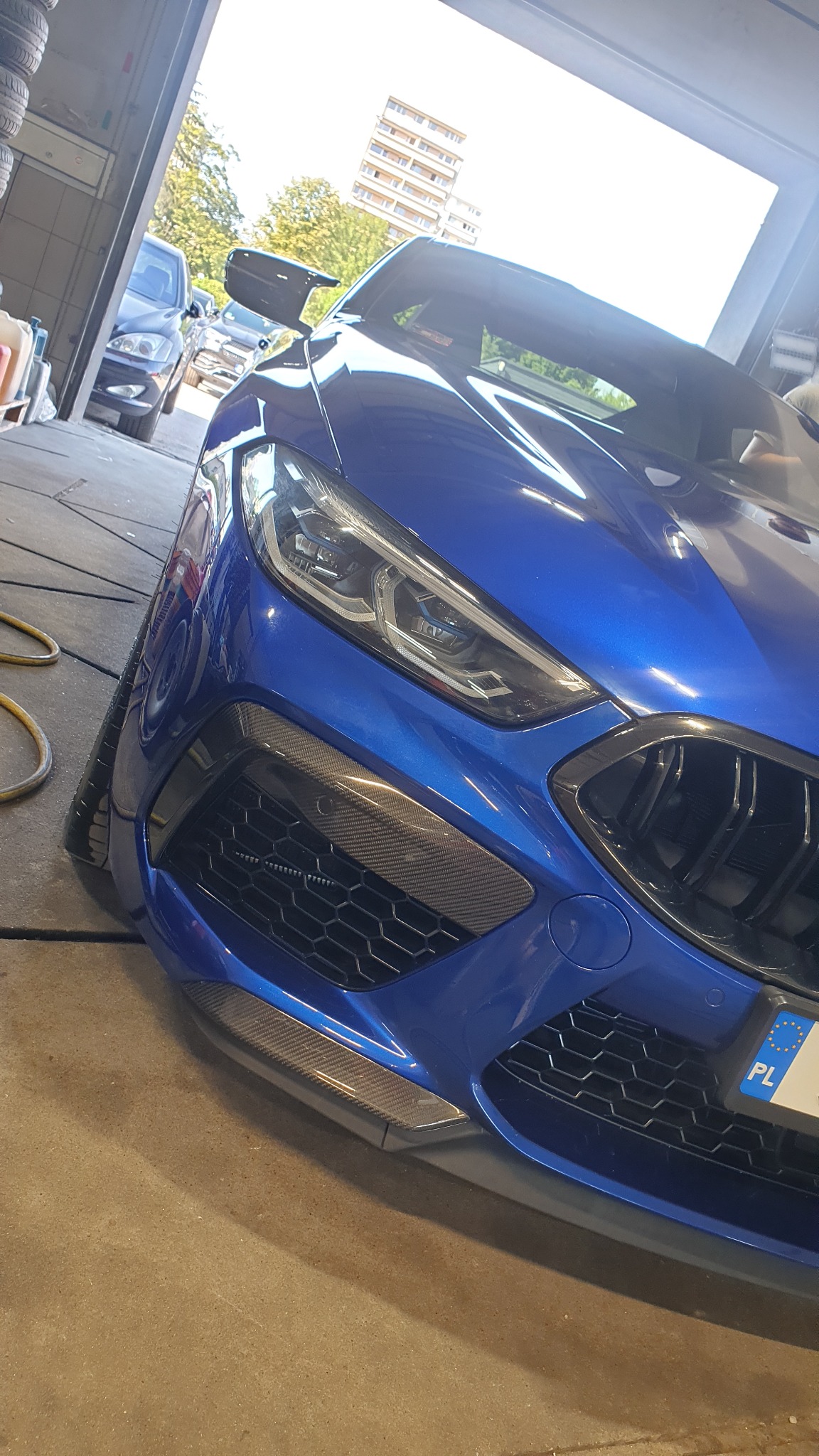 Niebieski sportowy samochód, widok z przodu, z elementami karbonowymi na zderzaku, zaparkowany w garażu.