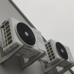 Dwa białe, zewnętrzne moduły klimatyzacyjne marki Bosch zamontowane na szarej ścianie budynku pod kątem, widoczne wsporniki montażowe.