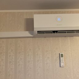 Jar-Mich jarosław Sokołowski Michał Niedźwiecki s.c. - Biała jednostka klimatyzacji marki Bosch zamontowana na ścianie z tapetą w delikatne wzory, obok wisi pilot sterujący.