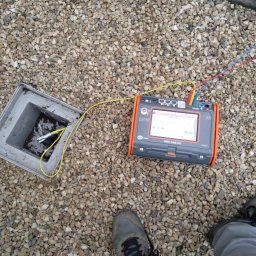 Jar-Mich jarosław Sokołowski Michał Niedźwiecki s.c. - Miernik MPI-540-PV podłączony do instalacji w skrzynce przyłączeniowej na tle żwirowego dachu, obok widoczna stopa w szarym bucie.