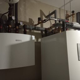 Jar-Mich jarosław Sokołowski Michał Niedźwiecki s.c. - Dwa białe urządzenia grzewcze marki Bosch, z widocznymi rurami, zaworami i manometrami, zamontowane na szarej ścianie.